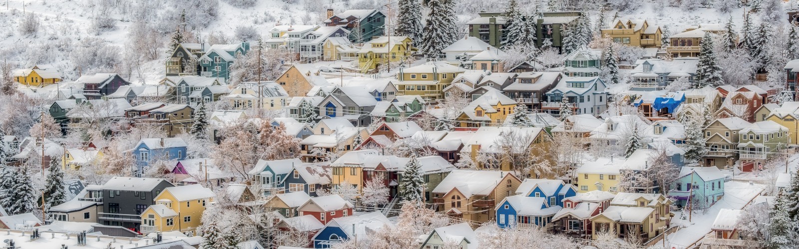 A snow-covered town with colorful houses nestled in a hilly landscape, surrounded by trees dusted in snow.