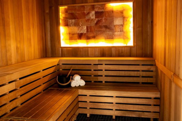 A wooden sauna room with a glowing salt wall, benches, and a bucket with towels on the right side.