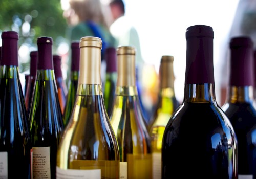 The image shows various wine bottles on display outdoors, with blurred figures in the background.
