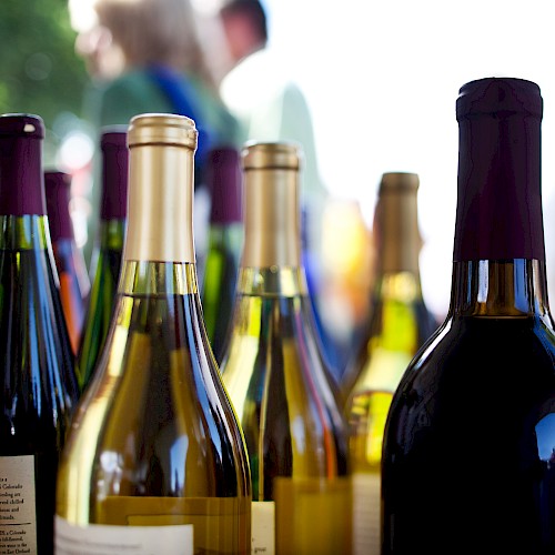 The image shows various wine bottles on display outdoors, with blurred figures in the background.