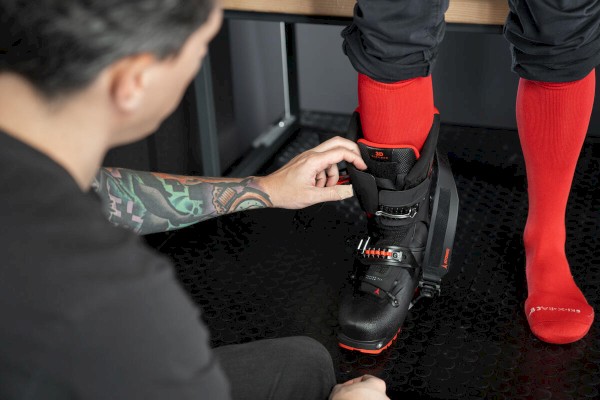 A person is adjusting a black ski boot on someone wearing red socks, with a focus on fitting the boot properly.