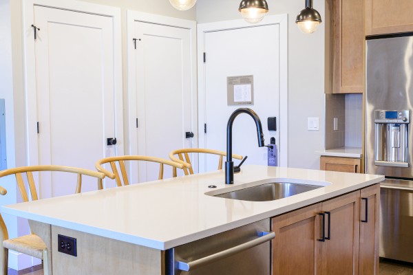 A modern kitchen with a center island, pendant lights, stainless steel appliances, wooden cabinets, and yellow chairs.