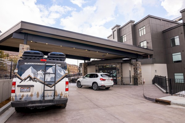 A hotel entrance with a covered driveway features a van and a white SUV parked outside in a modern setting.