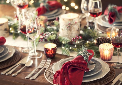 A festive table setting with plates, red napkins, wine glasses, candles, evergreen garlands, and holiday decor—ready for a celebration.