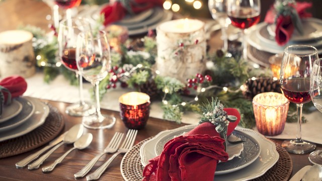 A festive table setting with plates, red napkins, wine glasses, candles, evergreen garlands, and holiday decor—ready for a celebration.
