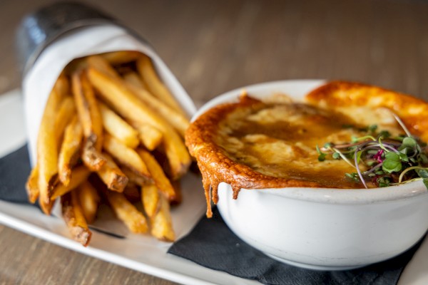 French fries are served alongside a bowl of cheesy, spicy soup garnished with microgreens on a wooden table.