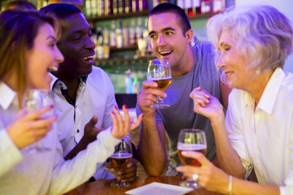 A group of friends enjoying drinks at a bar, laughing and chatting around a table with wine glasses and a bartender vibe.