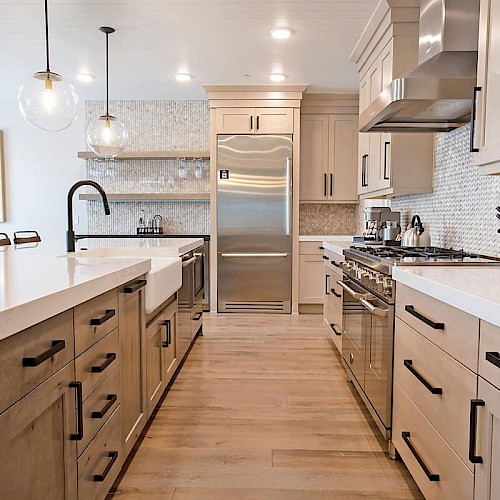 A modern kitchen with light wood cabinets, a large island, stainless steel appliances, pendant lights, and a clean, bright design.