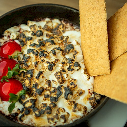 A creamy dip topped with cherry tomatoes, herbs, and seeds in a bowl, with crispy tortilla chips on the side.