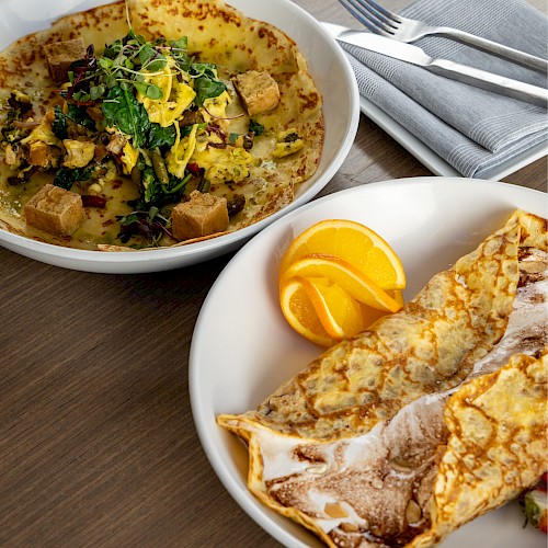 A hearty potato and herb curry topped with greens, and a stacked crepe with a lemon wedge on the side, plated for a cozy meal.