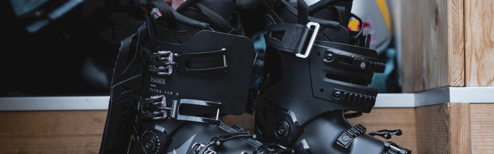 Snowboard boots with buckles inside a wooden doorway, labeled Atomic, black and sturdy, with a helmet visible in the background.