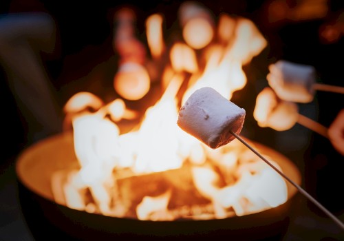 Toasted marshmallows roasting over a campfire, warm glow and blurred background, cozy outdoor dessert vibes.