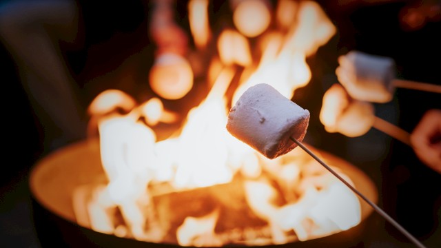 Toasted marshmallows roasting over a campfire, warm glow and blurred background, cozy outdoor dessert vibes.
