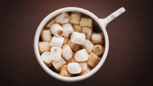 A white mug filled with hot chocolate topped with fluffy marshmallows, snowy squares dusted with cocoa.