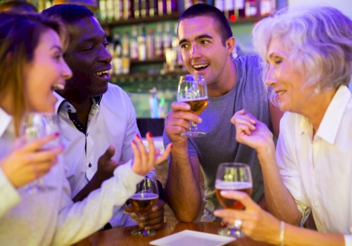 A group of friends at a bar, smiling and chatting, each holding a drink and enjoying a lively evening together.