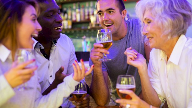 A group of friends at a bar, smiling and chatting, each holding a drink and enjoying a lively evening together.