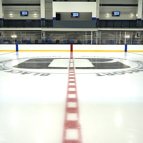 An ice hockey rink with red center line, blue lines, and team logos on the ice.