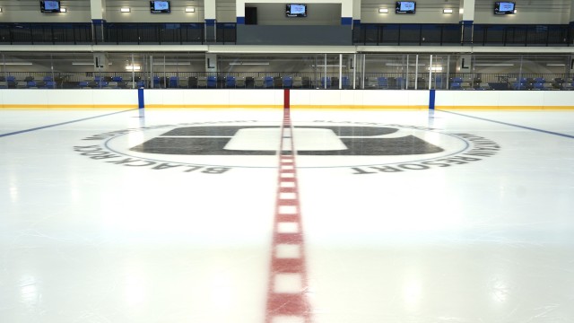 An ice hockey rink with red center line, blue lines, and team logos on the ice.