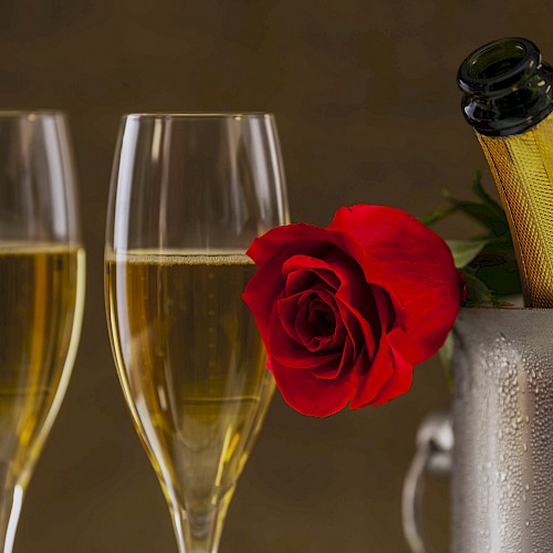 Two champagne flutes, a red rose, and a champagne bottle in a cooler, suggesting a celebratory moment.