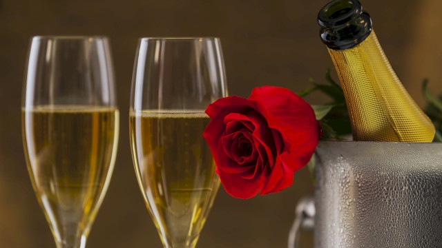 Two champagne flutes, a red rose, and a champagne bottle in a cooler, suggesting a celebratory moment.