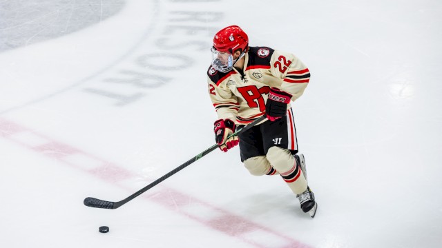 A hockey player in jersey number 22, wearing a red helmet, controls the puck on the ice rink.